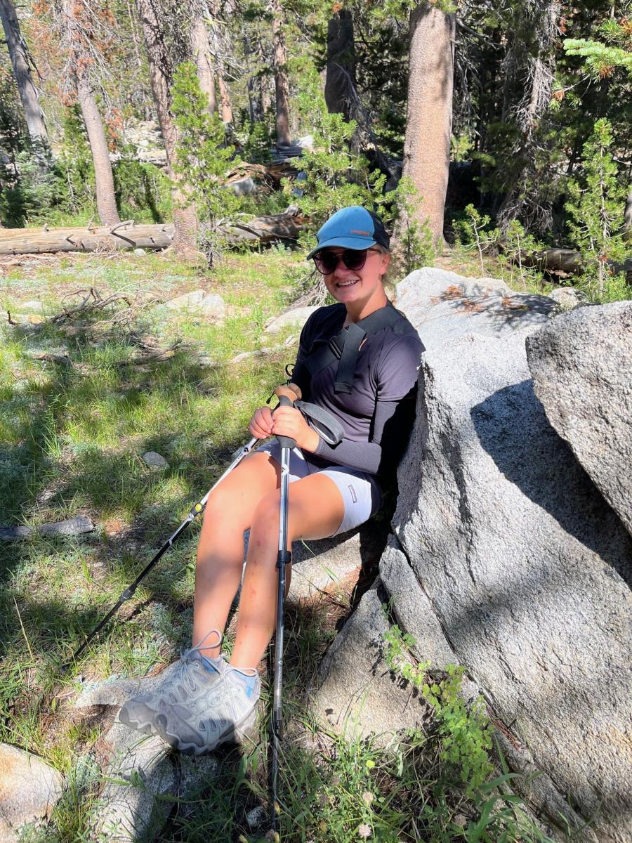 woman sitting on a large slab of rock and holding hiking poles